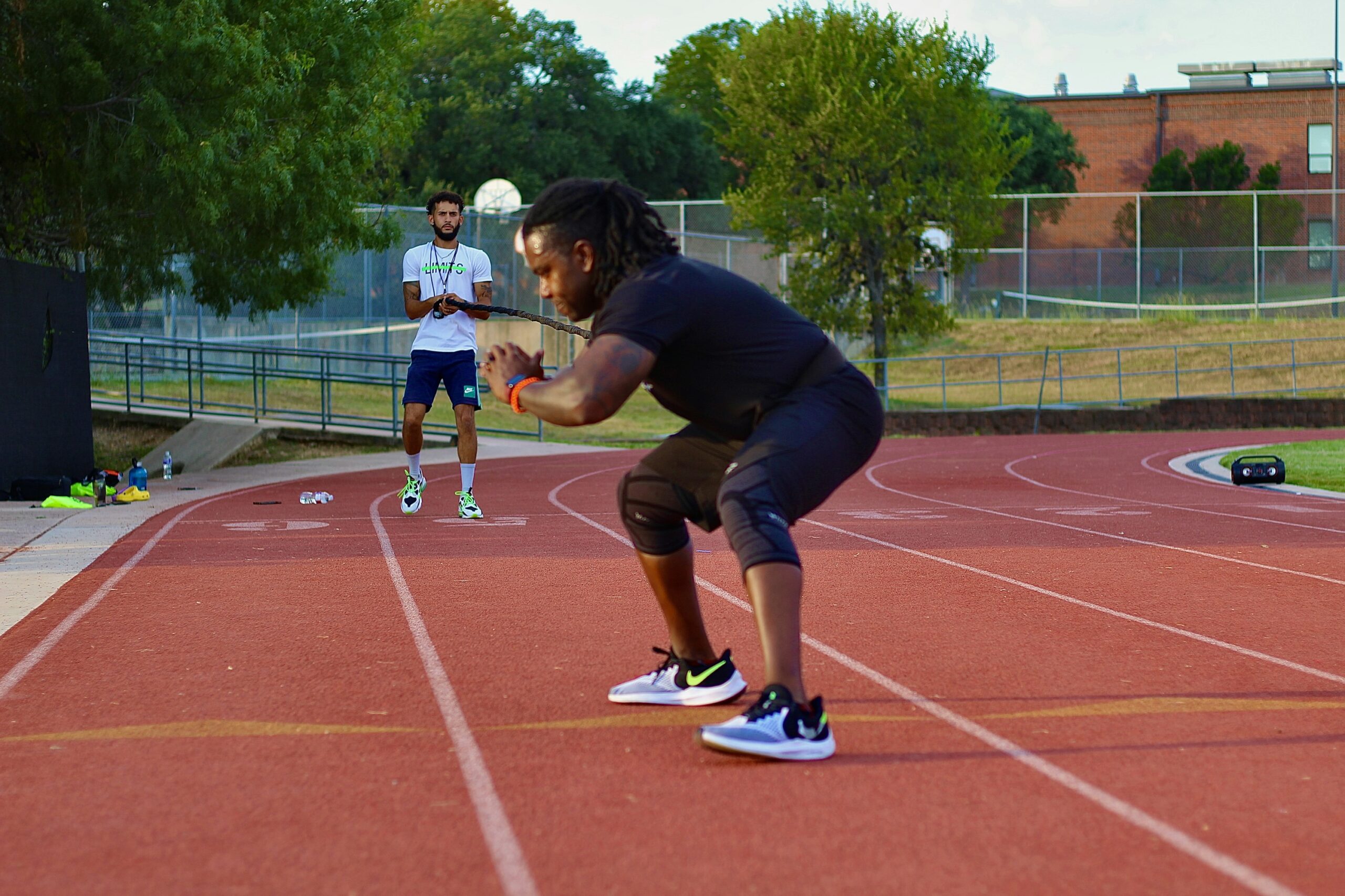 赤い陸上トラックでトレーニングをする人と、その動きを見守る人