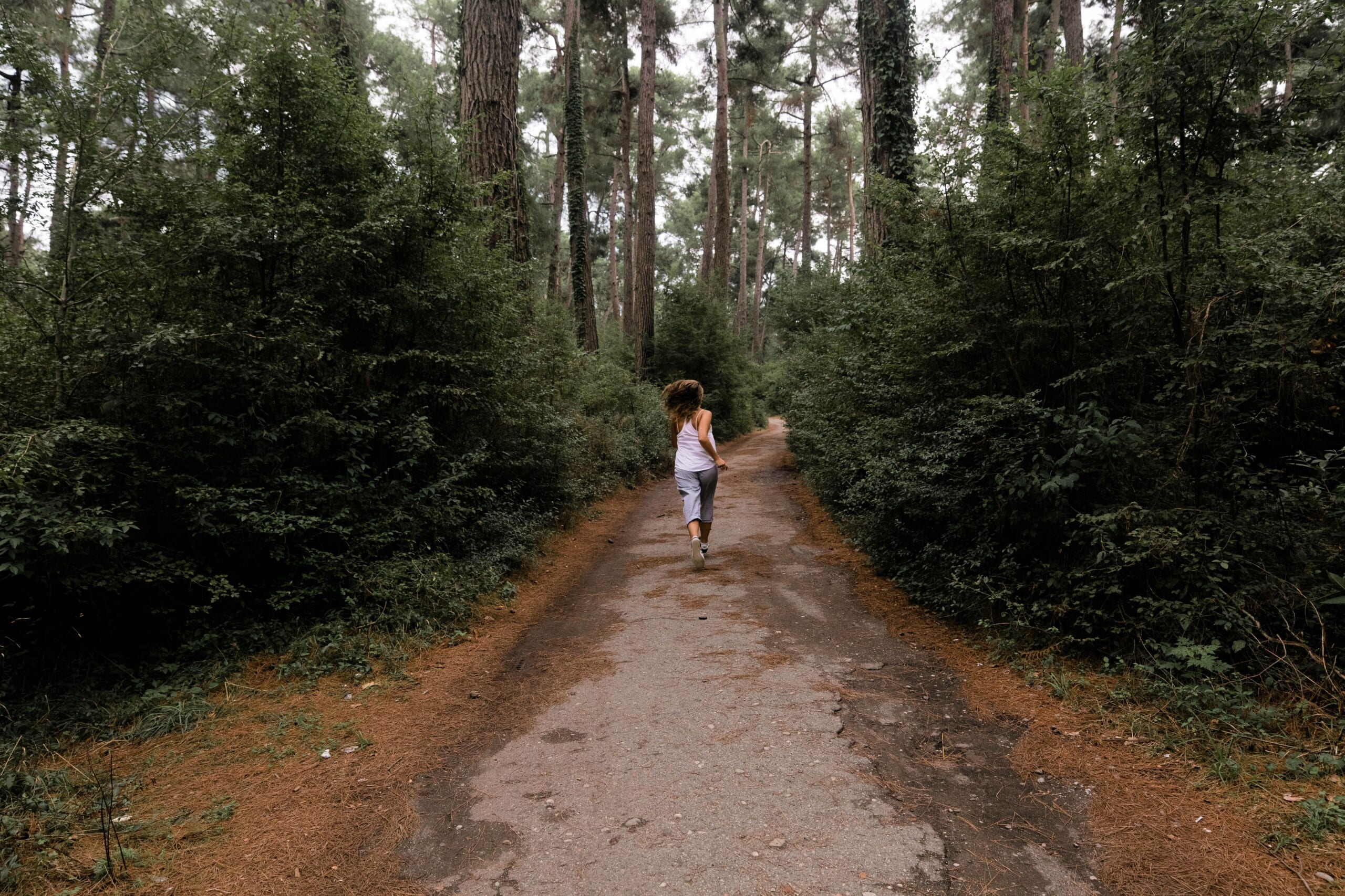 緑に囲まれた森の道を走る女性の後ろ姿