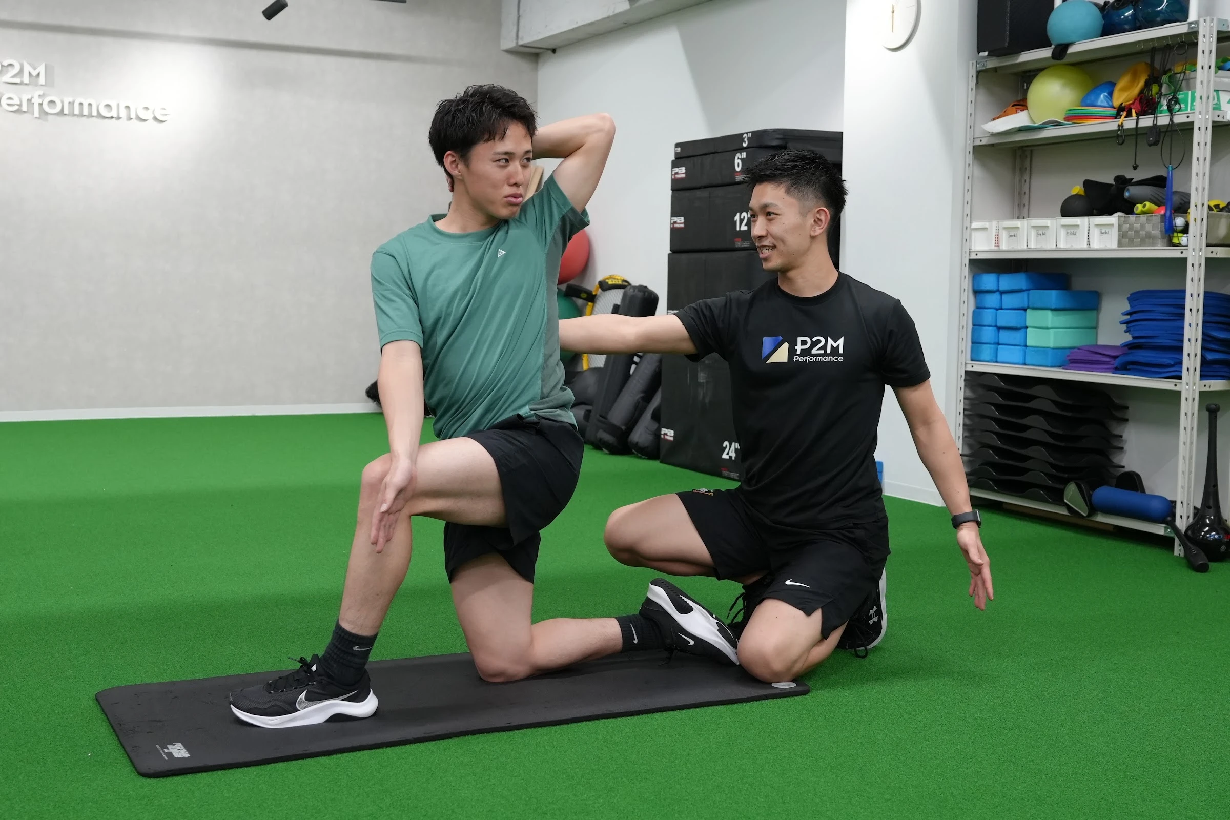 P2M Performanceの室内で、トレーナーのサポートを受けながら片膝立ちで上半身を動かす利用者